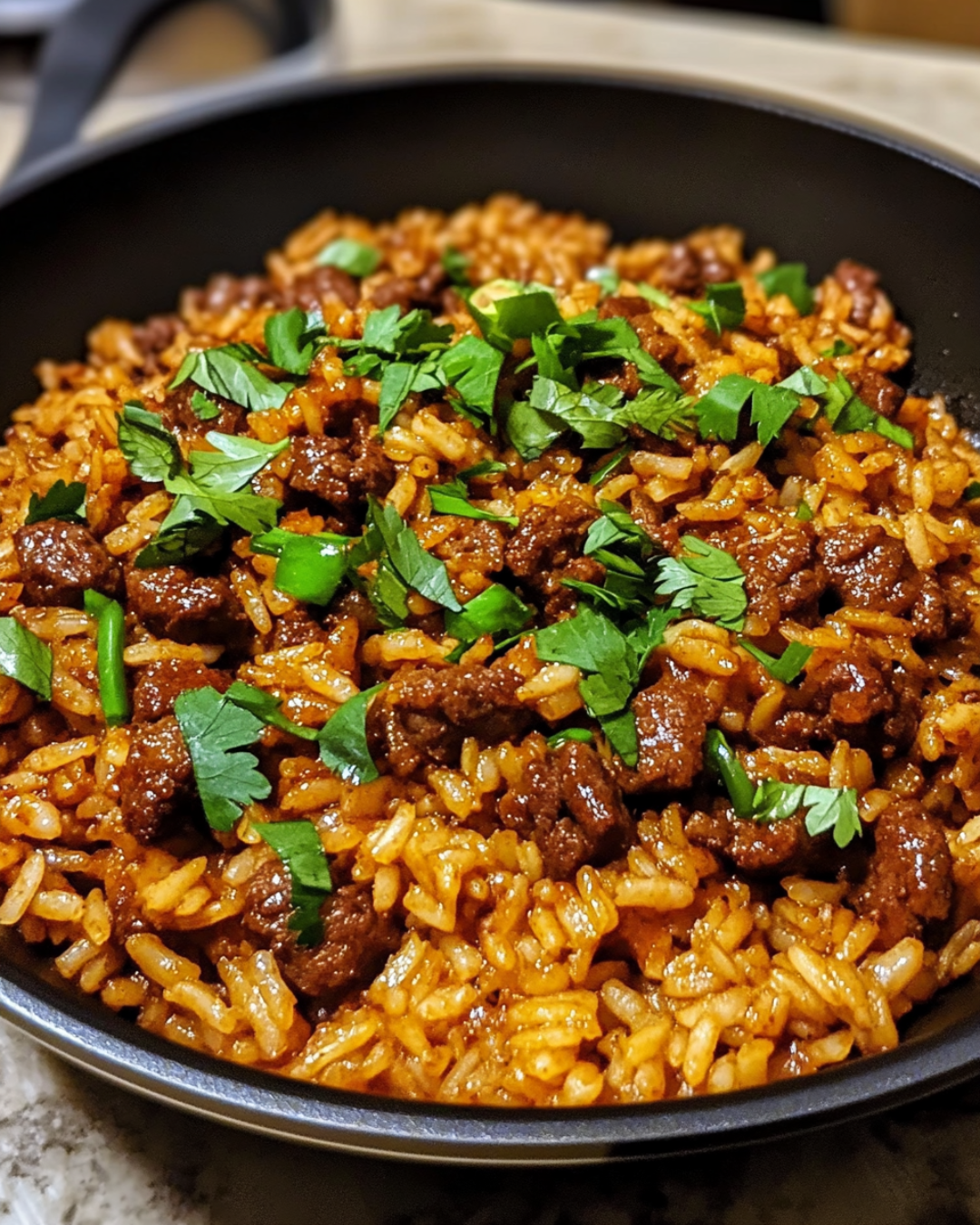 A delicious bowl of smoky honey chili beef rice, garnished with fresh cilantro and lime wedges, served in a skillet.