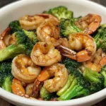 A plate of stir-fried shrimp and broccoli with a savory garlic-ginger sauce, served over steamed rice.