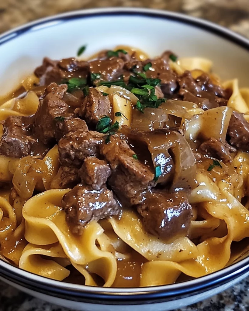 A bowl of creamy French Onion Beef and Noodles with caramelized onions, tender beef, and melted cheese, garnished with fresh parsley.