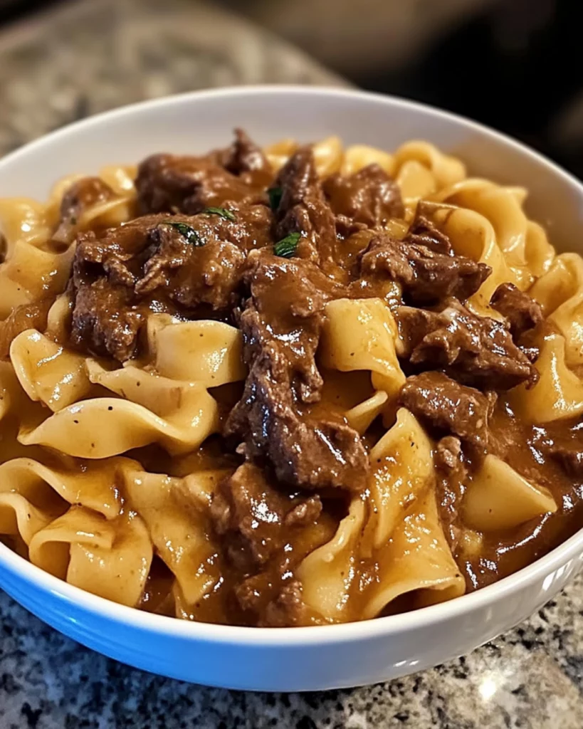 A bowl of creamy French Onion Beef and Noodles with caramelized onions, tender beef, and melted cheese, garnished with fresh parsley.
