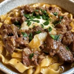 A bowl of creamy French Onion Beef and Noodles with caramelized onions, tender beef, and melted cheese, garnished with fresh parsley.
