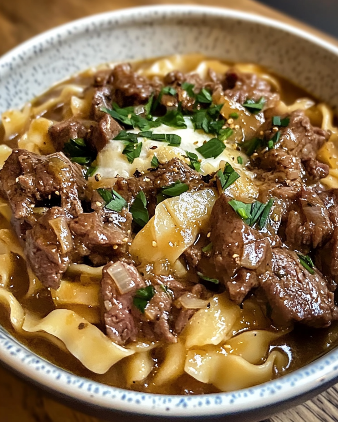 A bowl of creamy French Onion Beef and Noodles with caramelized onions, tender beef, and melted cheese, garnished with fresh parsley.
