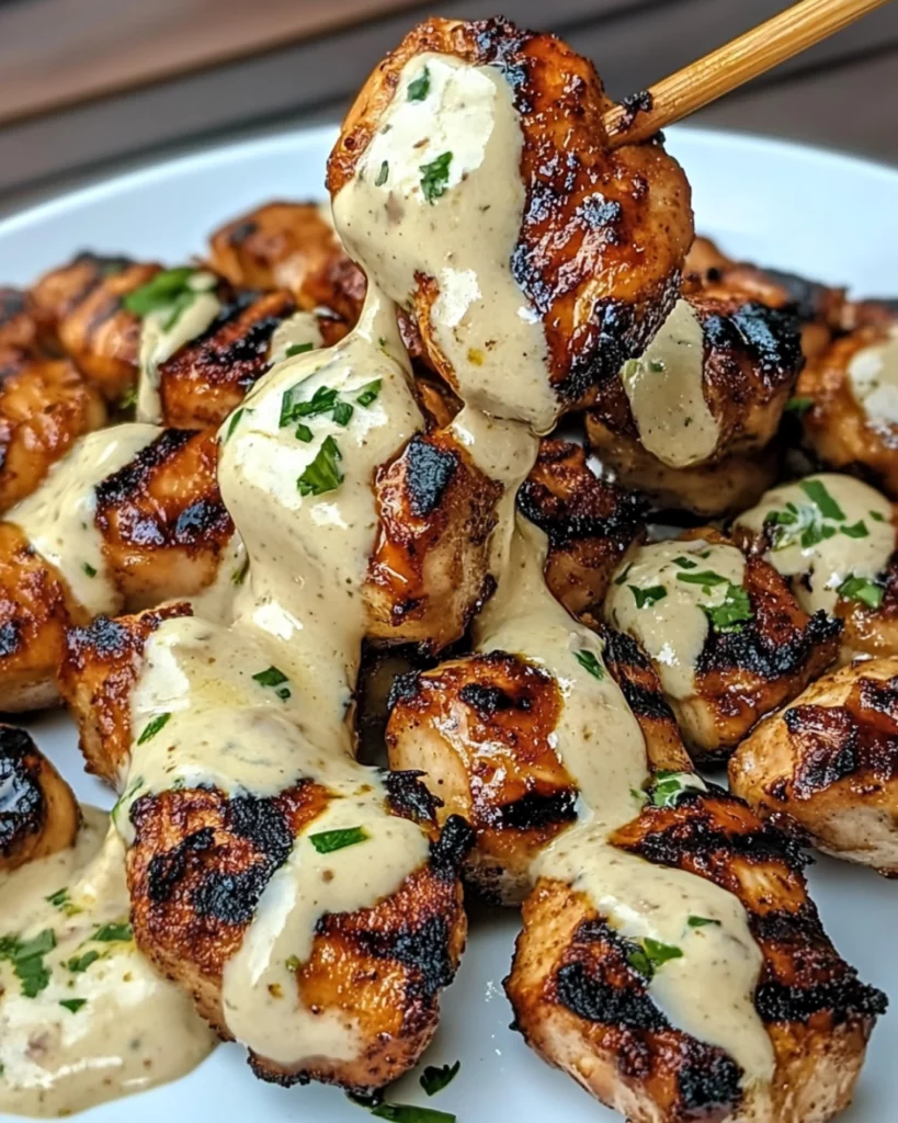 A plate of juicy grilled chicken bites drizzled with creamy garlic sauce, garnished with parsley and served with a side of rice.