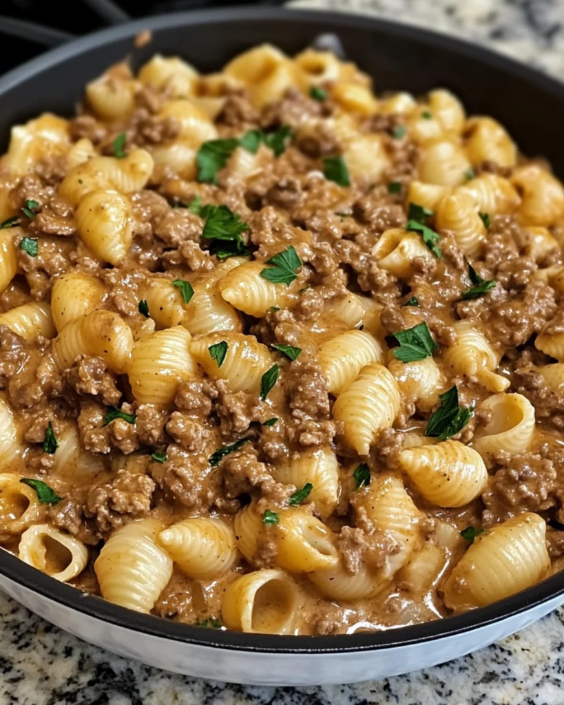 A bowl of creamy beef and pasta shells topped with fresh parsley and melted cheese, served in a white dish.