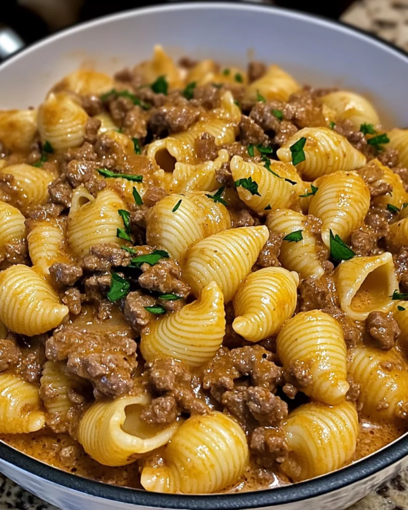 A bowl of creamy beef and pasta shells topped with fresh parsley and melted cheese, served in a white dish.