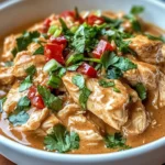 A bowl of Slow-Cooked Thai Peanut Chicken served over jasmine rice, garnished with peanuts, cilantro, and lime wedges.